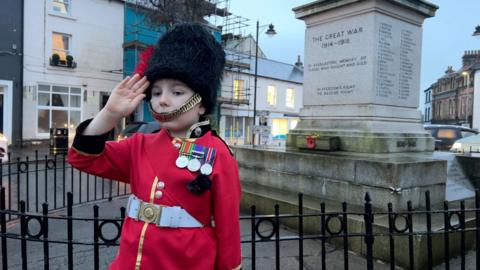 Frank, boy in soldier's outfit. He wears a bearskin hat and red uniform with medals on.