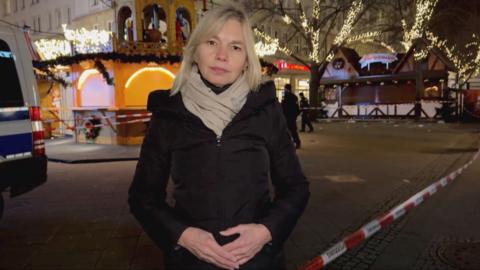 Bethany Bell wearing coat and scarf stands in the Christmas market which is cordoned off by police tape