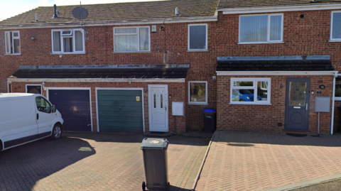 A red brick terraced house with a white door and a green and dark blue garage. 