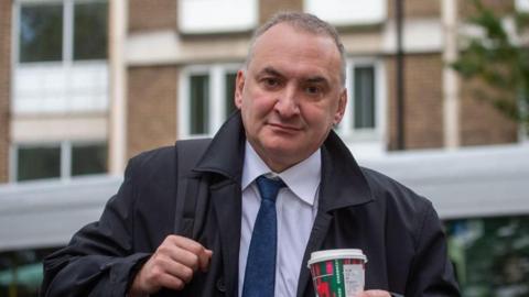 Sir Chris Wormald holding a coffee cup as he arrives at the Covid inquiry in London