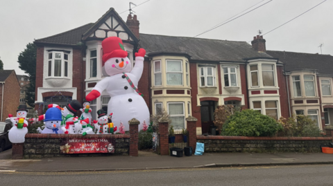 The outside of the Swindon house where 10 inflatable snowmen in different hats and scarves sit crammed in, one is much larger than the others and the top of it nearly reaches the roof of the house