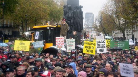 Crowd of protesters  holding banners including two on a yellow tractor a tractor holding banners stand in Whitehall in London