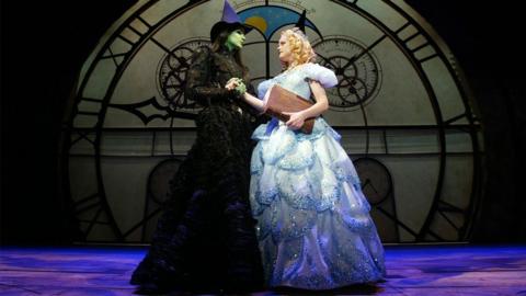 Elphaba and Glinda from Wicked on stage surrounded by the Broadway set.