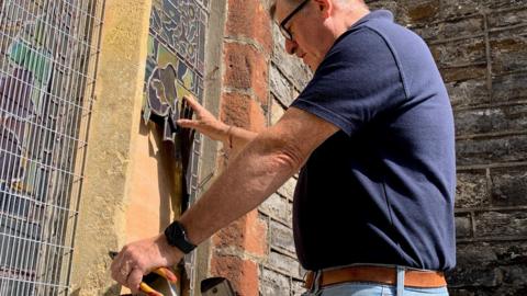 The Reverend Andrew Johnson examines the damage to a stained-glass window.