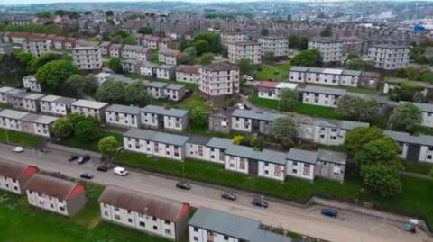 Aerial view of rows of houses and flats, with cars on roads.