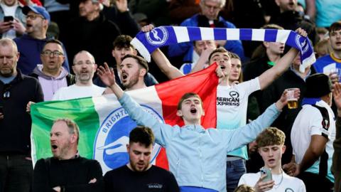 Supporters of Brighton & Hove Albion during the UEFA Europa Round of 16 first leg match between AS Roma and Brighton & Hove Albion at Stadio Olimpico on 7 March 2024 in Rome, Italy. Supporters have their arms in the air and appear to be chanting. 