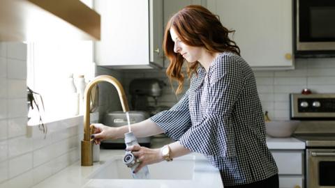 Women with red hair fills a bottle with water from the tap