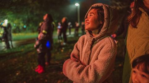 A child stands with their younger sibling and parents outdoors, wrapped up warm, looking up at the night sky.