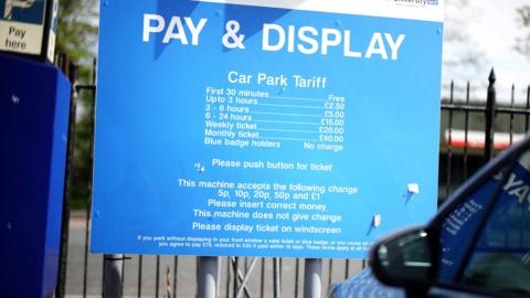 A Pay & Display blue hospital parking tariff board with white writing for payment amount.