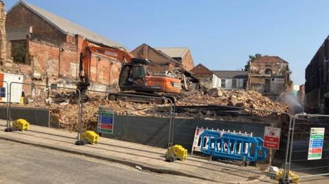 A orange digger sat on top of a demolished building