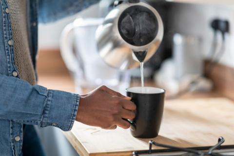 Person pouring water from a kettle into a mug