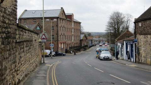 Street lined with stone buildings and cars parked on the side of the road.