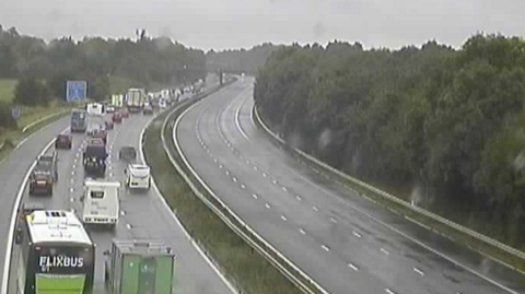 Traffic camera image of the M5 in Gloucestershire. One side of the carriageway is clear of vehicles, while the other has a long queue of traffic. 