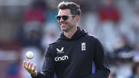 James Anderson tosses a white ball in the air while on coaching duties for England