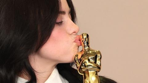 Close-up of singer Billie Eilish kissing her Oscar statuette. Her shoulder-length dark hair frames her face.