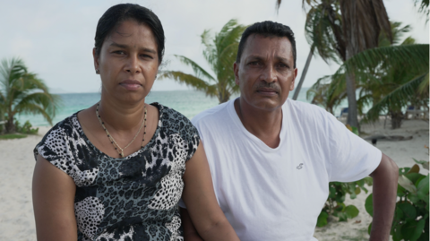 Maneshwary and Suresh Seesahai sitting on the beach in Anguilla, with the sand, sea and palm trees in background