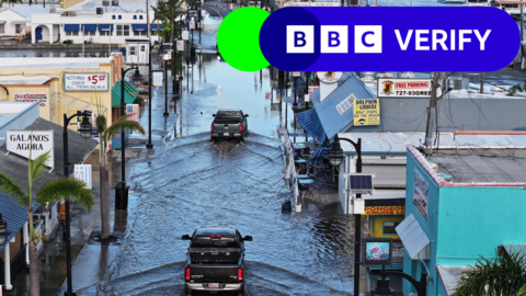 Cars in Florida drive through a street flooded with water after Hurricane Helene.