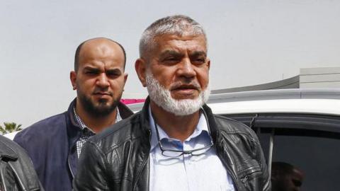 (Front L to R) Hamas ranking members Khalil Al-Hayya and Rawhi Mushtaha stand outside the VIP hall at the Rafah border crossing with Egypt in the southern Gaza Strip on March 15, 2021 - both men are wearing shirts and leather jackets, and Mushtaha has glasses hanging from his neck. 