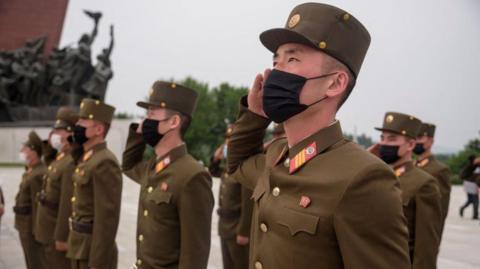 North Korean soldiers wearing facemasks salute as they pay their respects to the country's former leaders in 2021