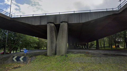 A huge flyover is held up by two concrete pillars. The image is taken from below.