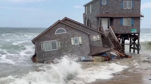 A wave splashes in front of a house that has collapsed into the sea