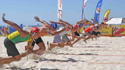 Competitors wearing colourful shorts, vests and swim caps ready to sprint on the sand at the Lifesaving World Championship