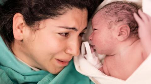 Mother lying down and cradling her newborn baby in hospital