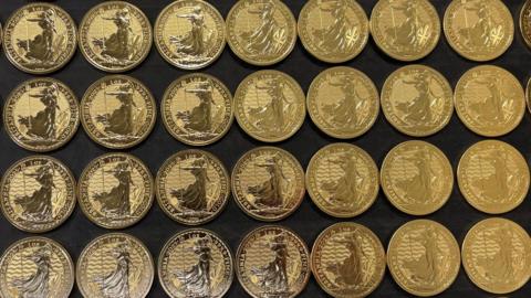 A tray of 24 carat gold bullion coins bearing the image of Britannia laid out side by side.