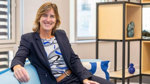 Dame Katherine Grainger smiles at the camera while sitting on a sofa