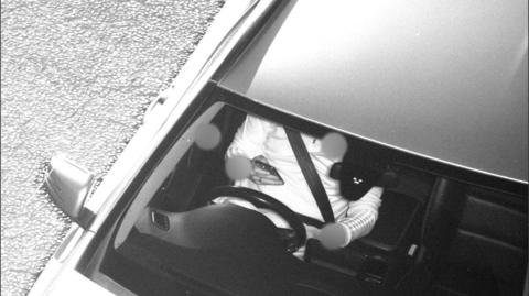 A driver on their mobile phone behind the wheel of a car, wearing a seatbelt