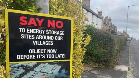 A large sign saying 'Say No to Energy Storage' at the entrance to a village street