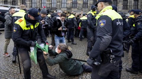 Dutch police detain a pro-Palestinian protester in Dam Square. The protester is wearing a face mask and lying on the ground while the policeman tries to take a Palestinian flag off her.