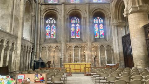 Inside Peterborough Cathedral, with stained glass windows and chairs facing the alter.