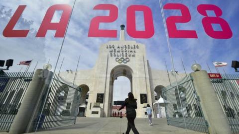 The entrance of Los Angeles Memorial Coliseum is reflected on a window that has "LA 2028" written on it