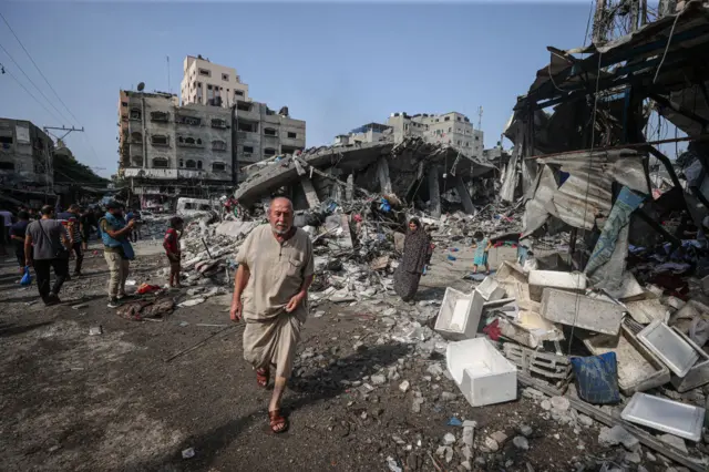 People walk on the street in Gaza next to the buildings destroyed by Israeli airstrikes