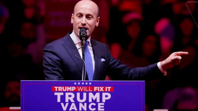 Stephen Miller speaking at the Trump rally at Madison Square Garden in late October, stood behind a lectern wearing a suit and pointing to the side