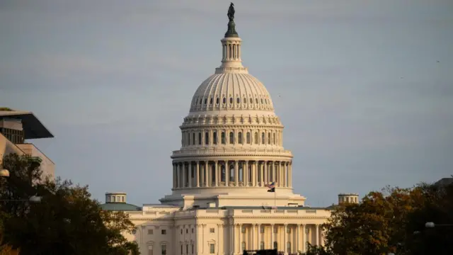 The Capitol building is seen in daylight, with the sun shining down over the large dome on the top of the white building.