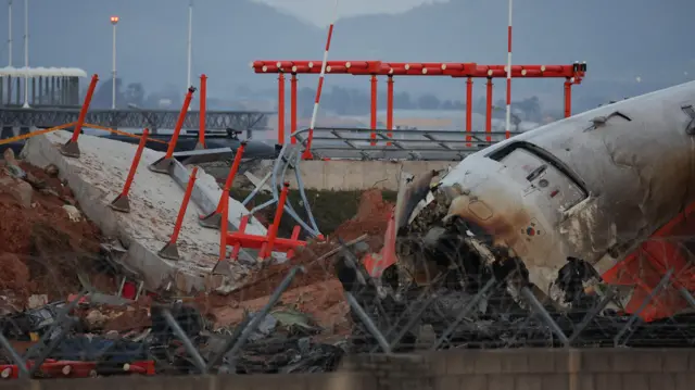 The wreckage of the Jeju Air aircraft that went off the runway and crashed at Muan International Airport lies near a concrete structure it crashed into, in Muan, South Korea