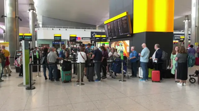 A queue of people looking up at notice boards in Heathrow airport