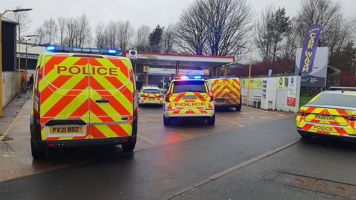 Five police vehicle at the scene at Gilwilly Industrial Estate in Penrith. There is a "car wash" sign next to where the vehicles are parked.