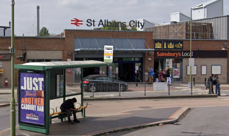 The main entrance to St Albans City train station with a bus stop in the foreground and a Sainsbury's local supermarket in the background.