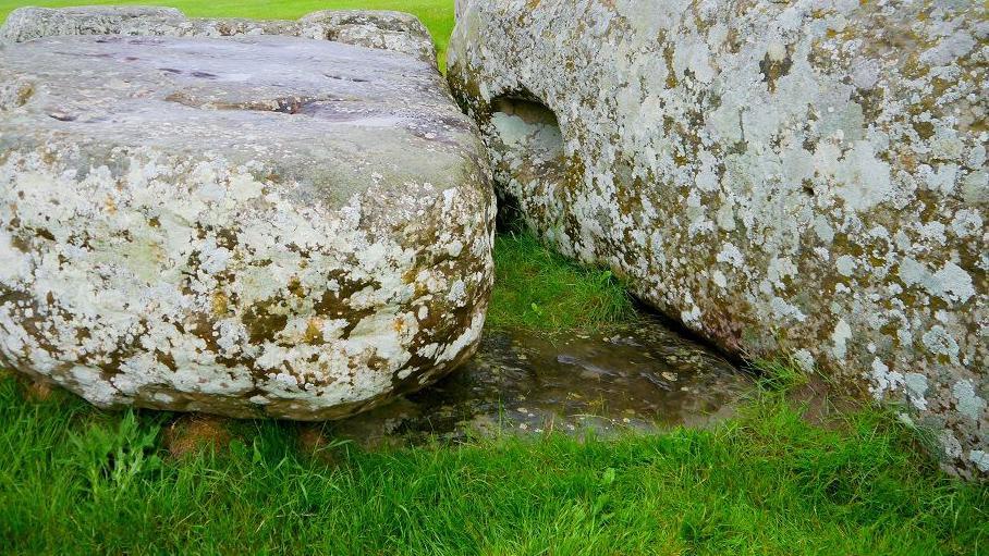 Two large stones lying on grass, with one partially buried underneath.