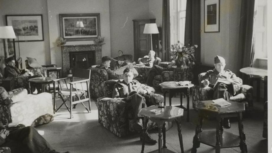 A black and white photo of the Canadians' New Beaver Club for Canadian soldiers on leave in London, showing one of the fine lounges where the men are sat reading