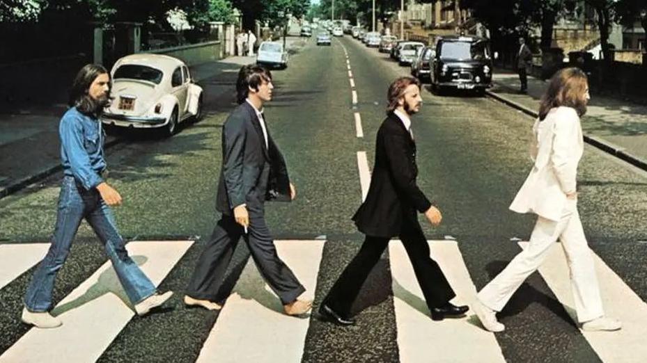 The Beatles' Abbey Road album cover shows four men, George Harrison, Paul McCartney, Ringo Starr and John Lennon, walking on a zebra crossing outside the recording studios in north London. It is a residential street with cars parked on either side of the road.