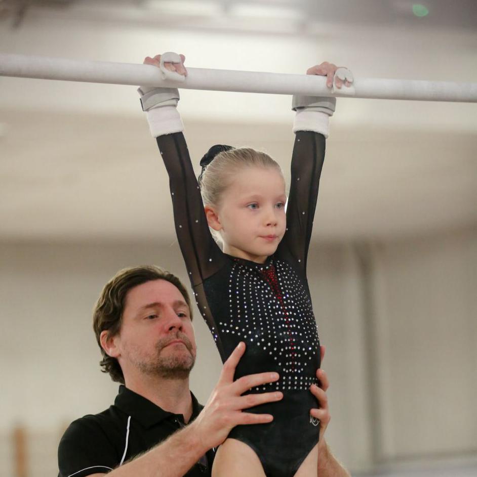 Dominic Brindle supports his daughter from the waist as she holds the gymnastics bar.