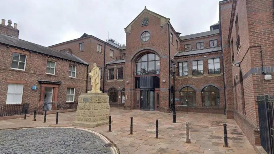 Carlisle Crown Court. It is a brown brick building with a statue outside.