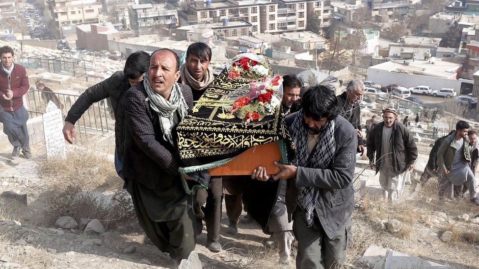 a group of men carrying a coffin up a dusty hill, with city buildings in the distance