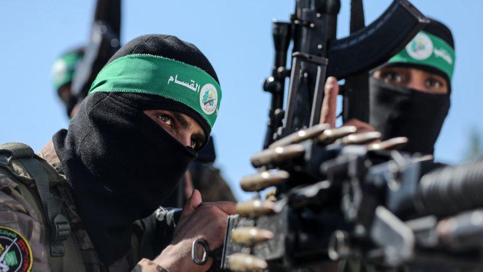 Hamas fighters wearing balaclavas hold weapons