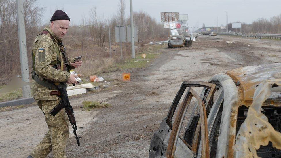 soldier stands by car and corpse (not shown)