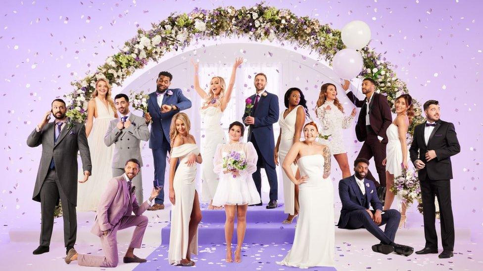 The cast of MAFS UK 2023 - a mix of the 16 contestants made up of eight grooms wearing suits and eight brides in white dresses. The cast are pictured on a purple background with confetti and a floral wedding arch